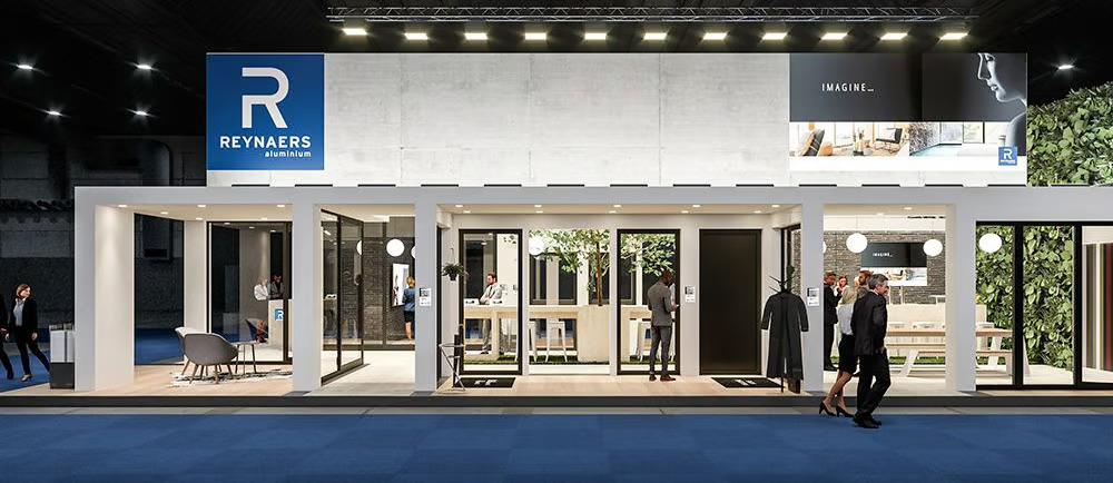 A large, modern exhibition stand for Reynaers Aluminium featuring a white minimalist structure with various glass doors and windows on display, set against a blue carpeted floor.