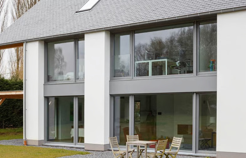 Modern two-story house with large glass windows and sliding doors, white exterior walls, and a grey tiled roof.